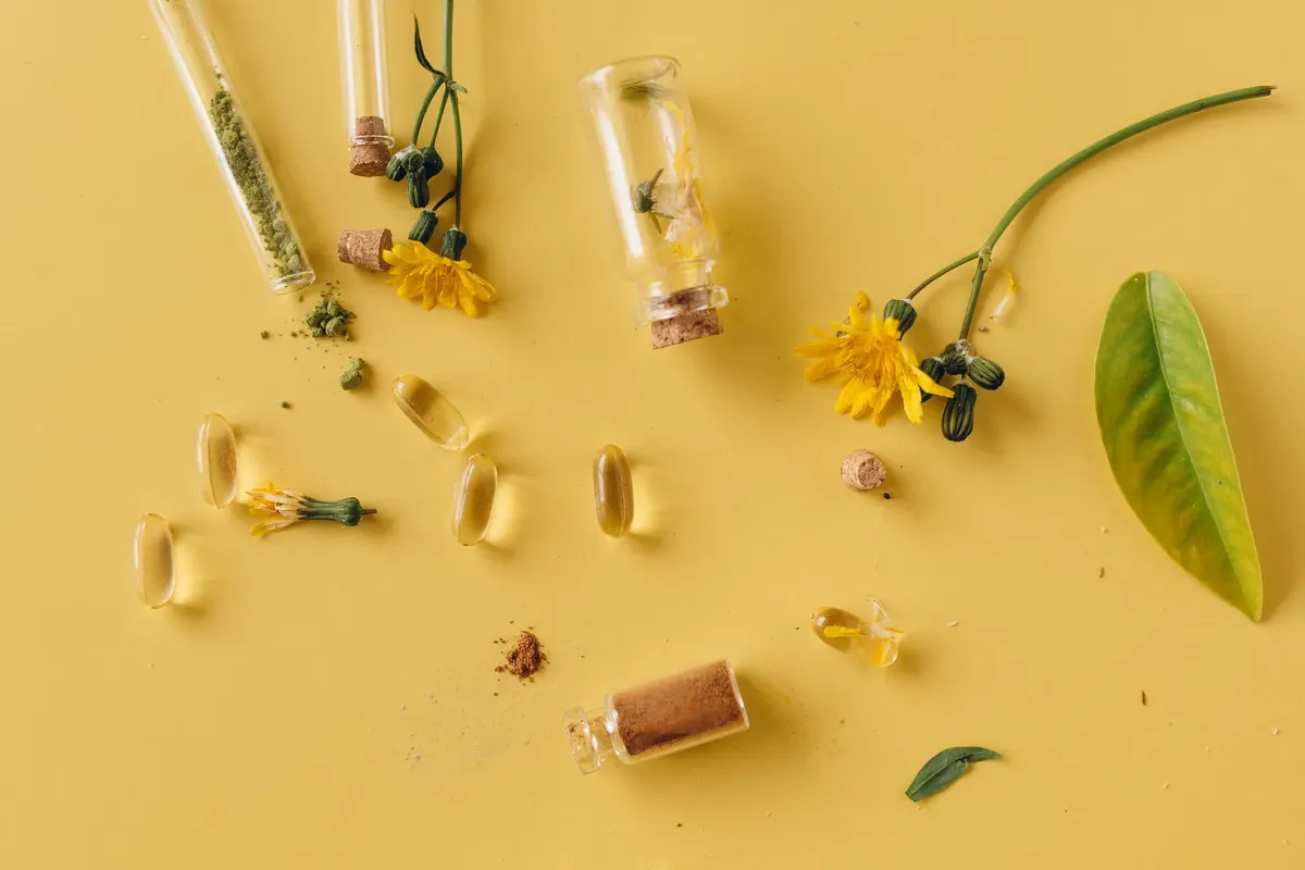 玻璃瓶、膠囊與花朵平鋪於活潑的黃色表面，象徵自然療法。