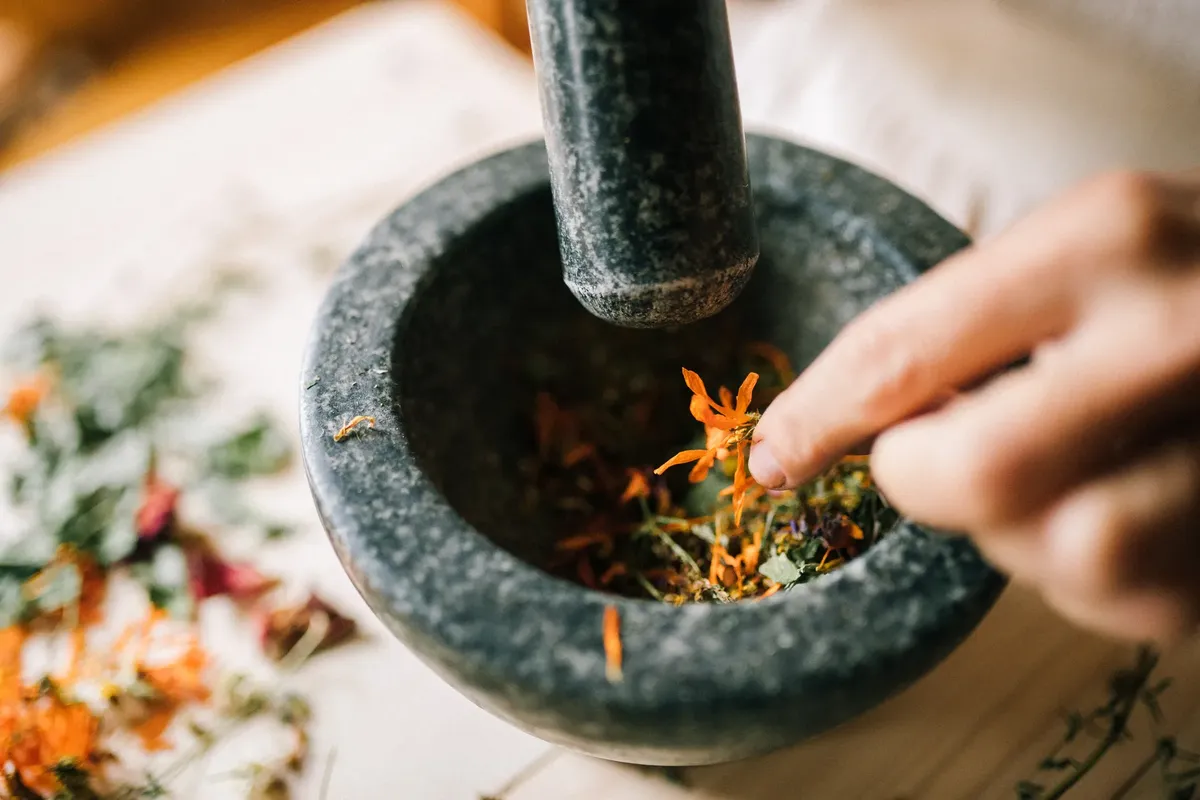 A hand crushes vibrant herbs in a stone mortar, blending natural ingredients.